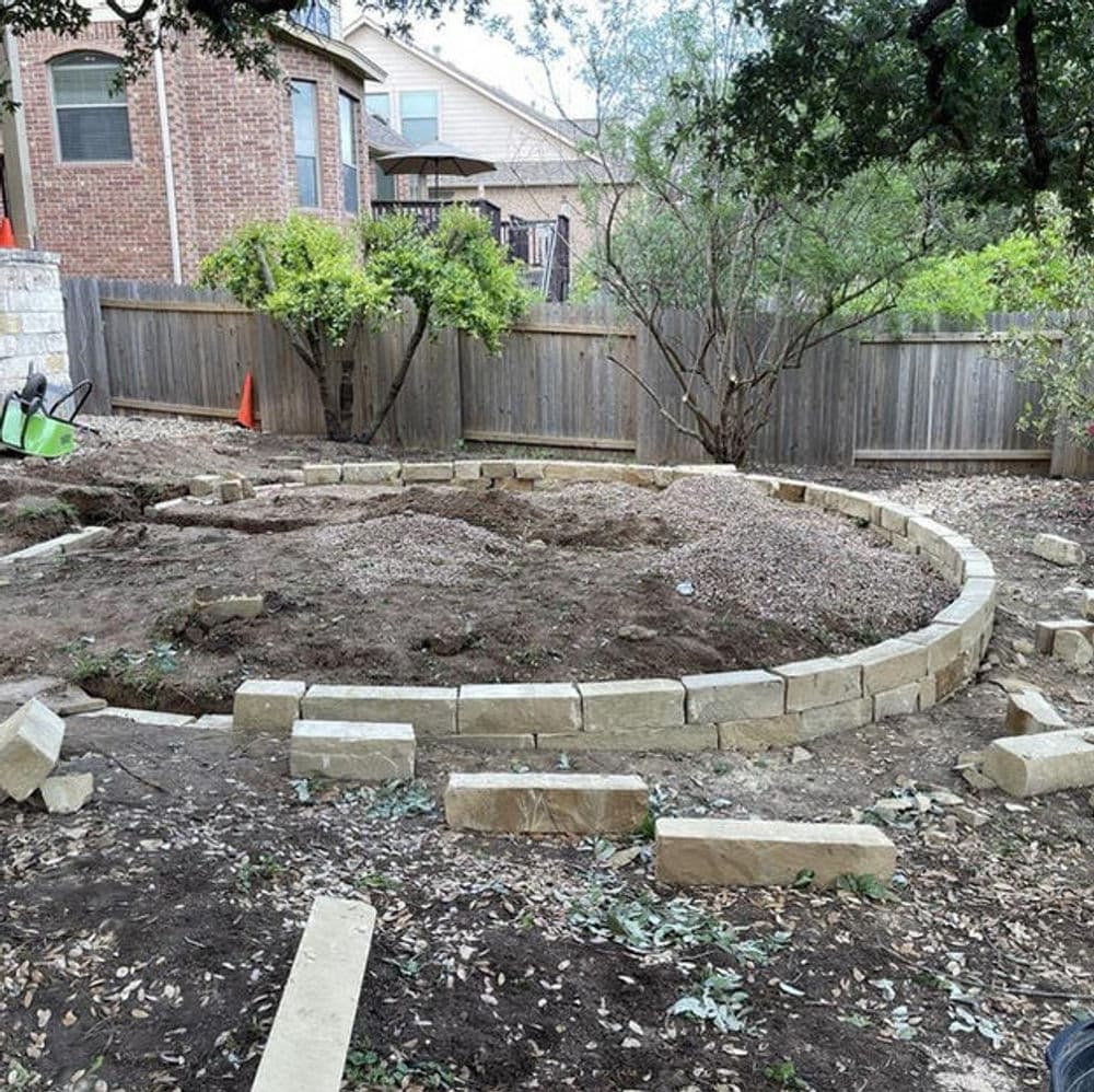 Backyard landscaping project with stone border, cleared soil, and plants in progress.